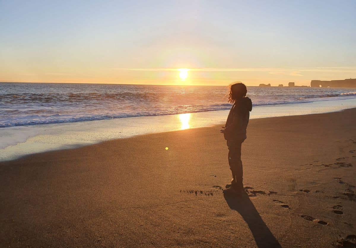 Teen standing on the shore of the Black Sand Beach at sunset in Iceland