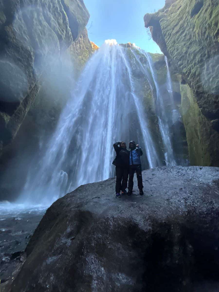 Teenagers in Iceland standing on a rock next to a gushing waterfall