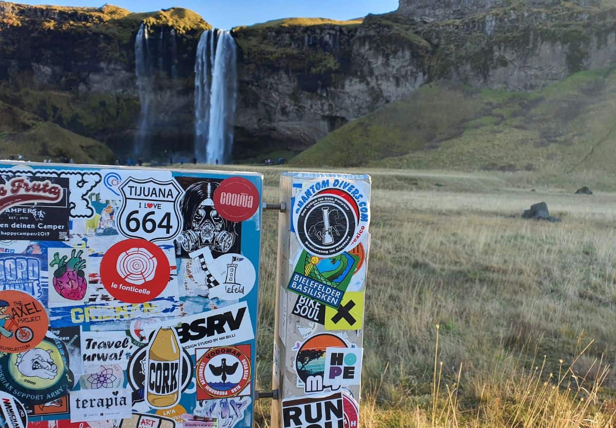 Picture of sticker covered stand with the waterfall, Seljalandfoss in the background
