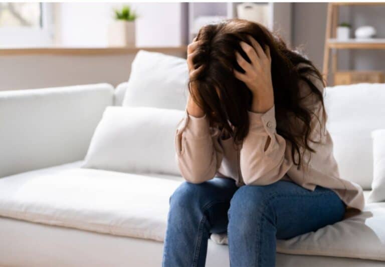 Woman sitting on couch with head in hands, distraught