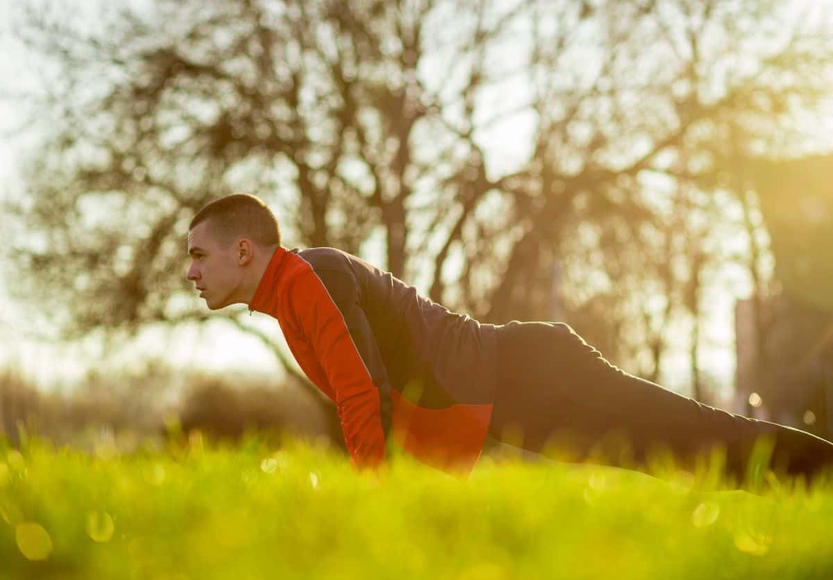 A teen in a sweatsuit doing pushups outside in the early morning light