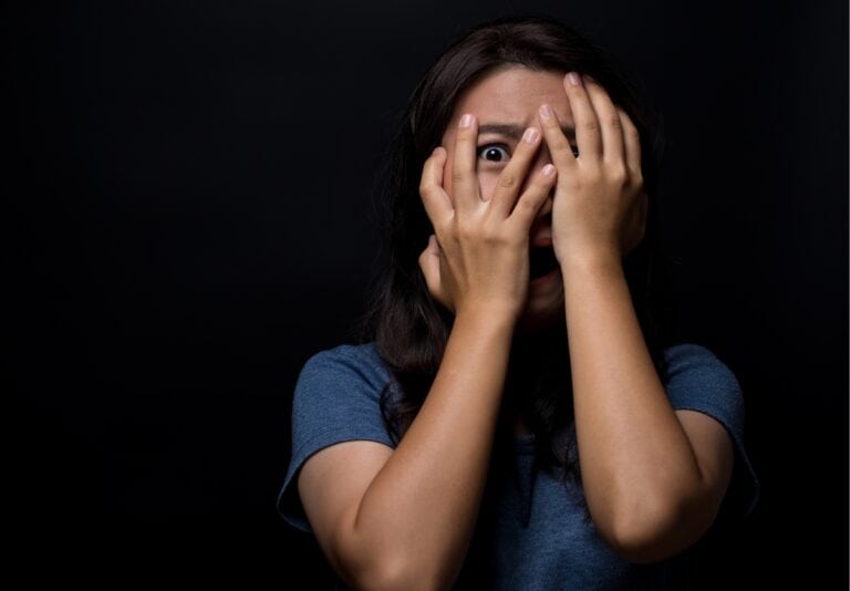 A scared teen girl with her hands covering her eyes