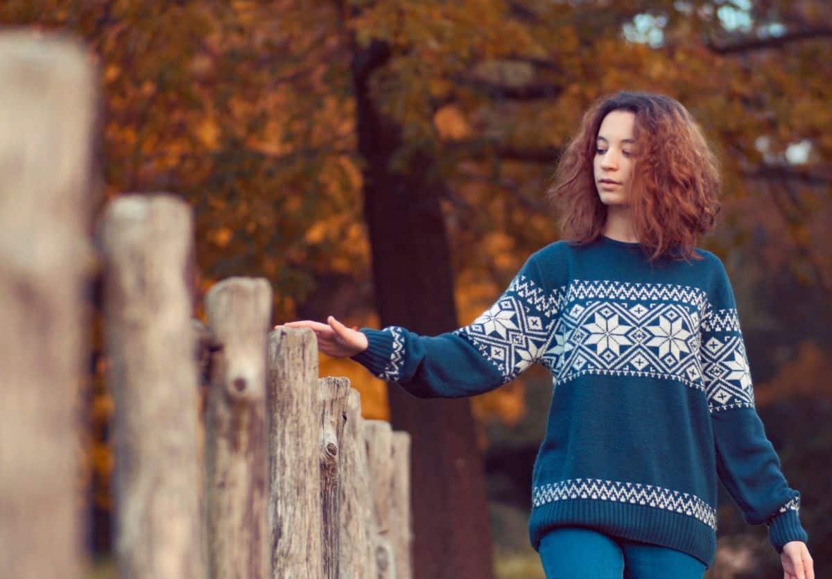 A white teenager in a sweater walking along a wooden fence