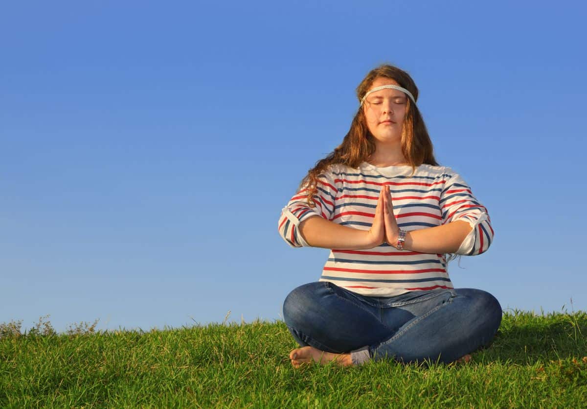 A white teenager with long hair sitting cross-legged in the grass meditating