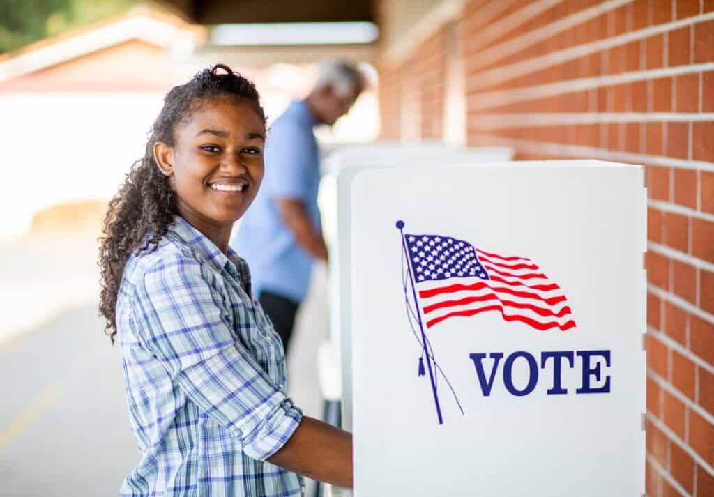 A Black teenage girl smiling as she votes.