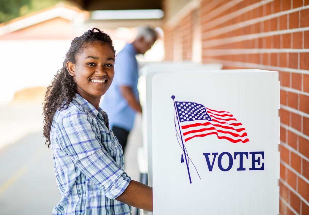 A Black teenage girl smiling as she votes.