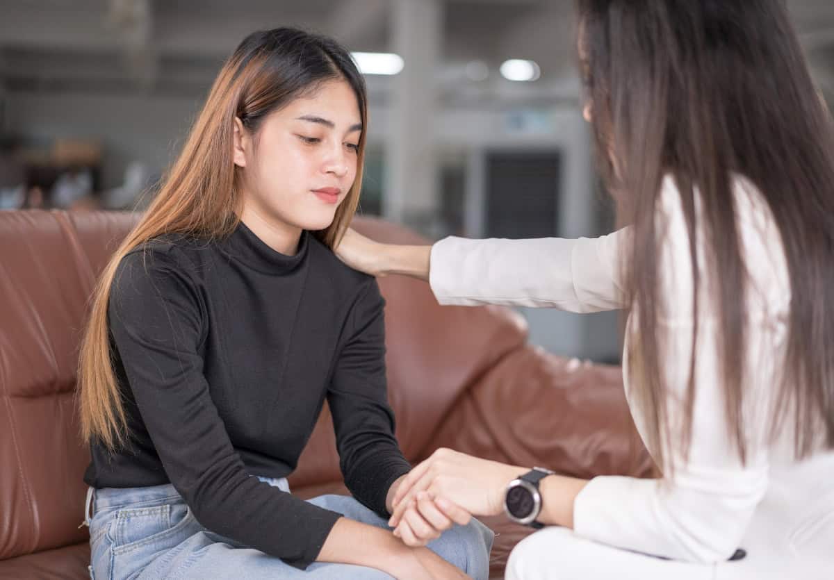 Teenager on couch looking solemn holding a counselors hand