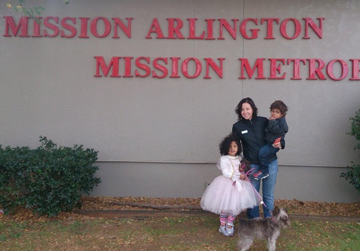 A mom with two toddlers and a dog standing in front of a Mission Arlington sign to volunteeron Thanksgiving