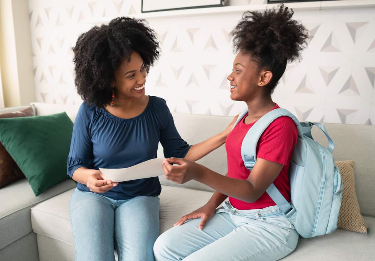 Teenage daughter sharing her good report card with her mom on a couch in the living room.