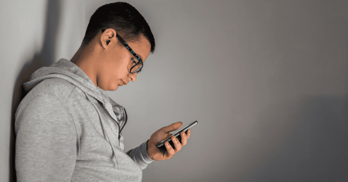 A teenage boy learning against a wall looking at his phone