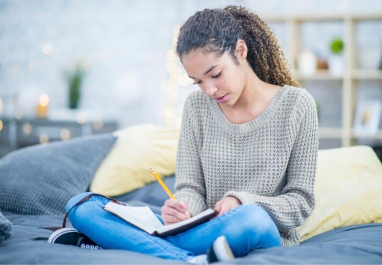 teen sitting cross-legged on her bed journaling